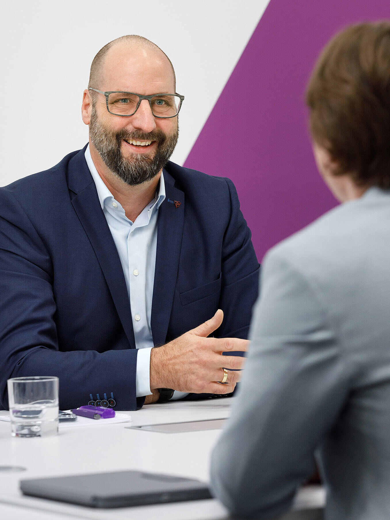 Lachende Person in einer Gesprächsituation mit einer von der Kamera abgewandten, anderen Person.