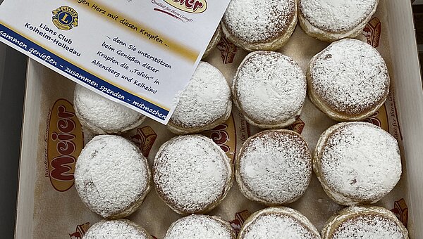 A full box of donuts with a flyer for the Lions Club.