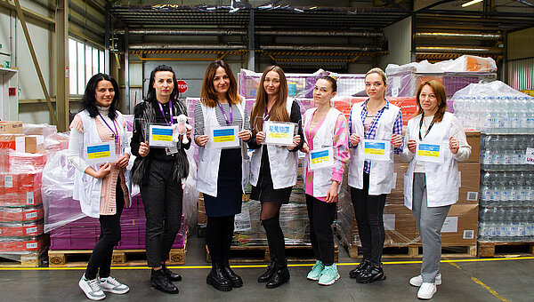 Employees holding Ukrainian flags in front of pallets of relief supplies