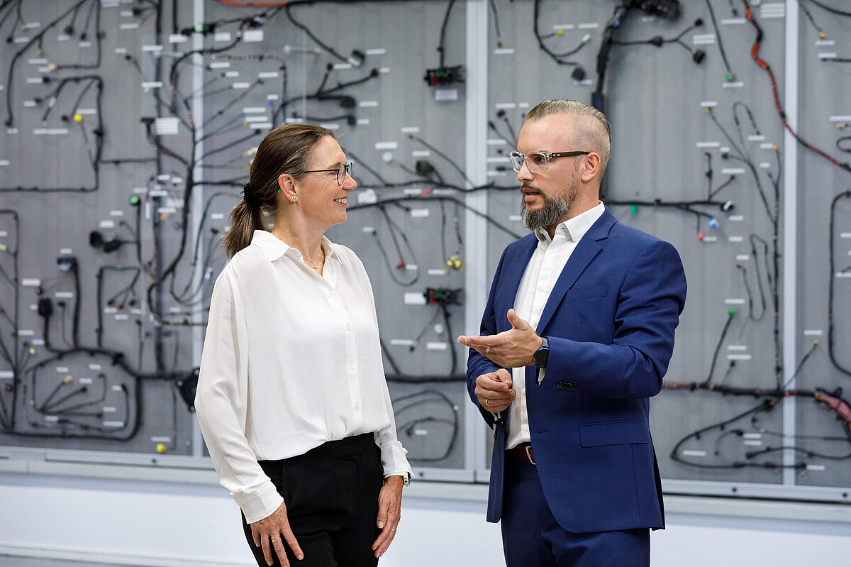 Gesprächssituation zwischen zwei Personen vor einem Bordnetz.