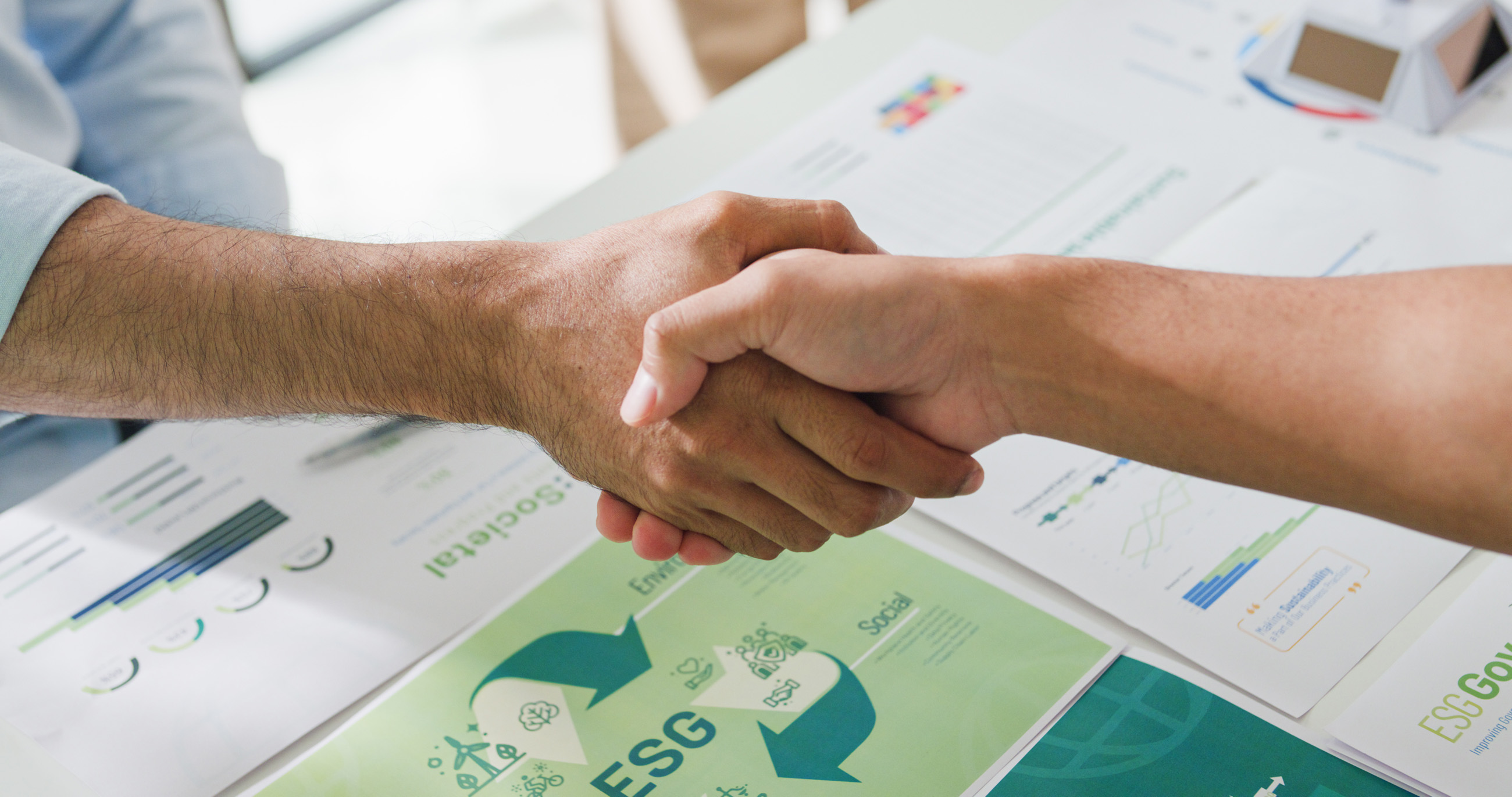 Zwei Hände, die sich über Formularen zum Thema "ESG" schütteln.